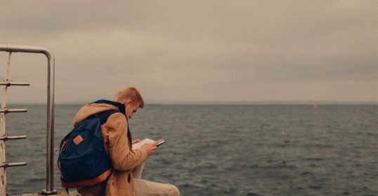 A man on a pier, uncertain about the book he is reading.