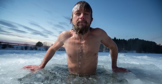 A bearded man is standing in an ice pool, showcasing human resilience.