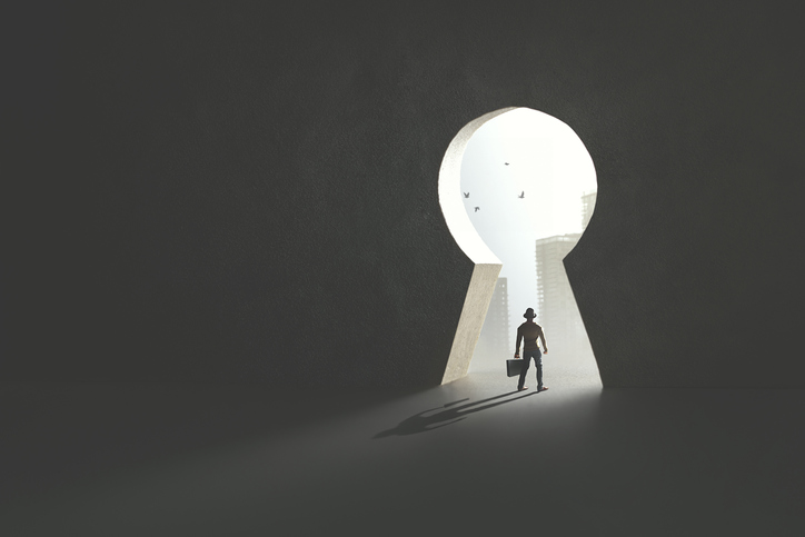 A businessman is navigating through a keyhole in a dark room, attempting to get out.