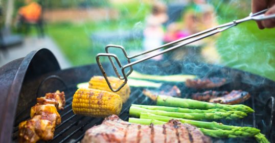 A grillmaster is flame-cooking a steak on a grill.