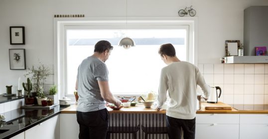 Two adults podcasting in a kitchen while preparing food.
