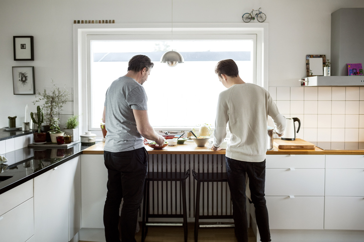 Two adults podcasting in a kitchen while preparing food.