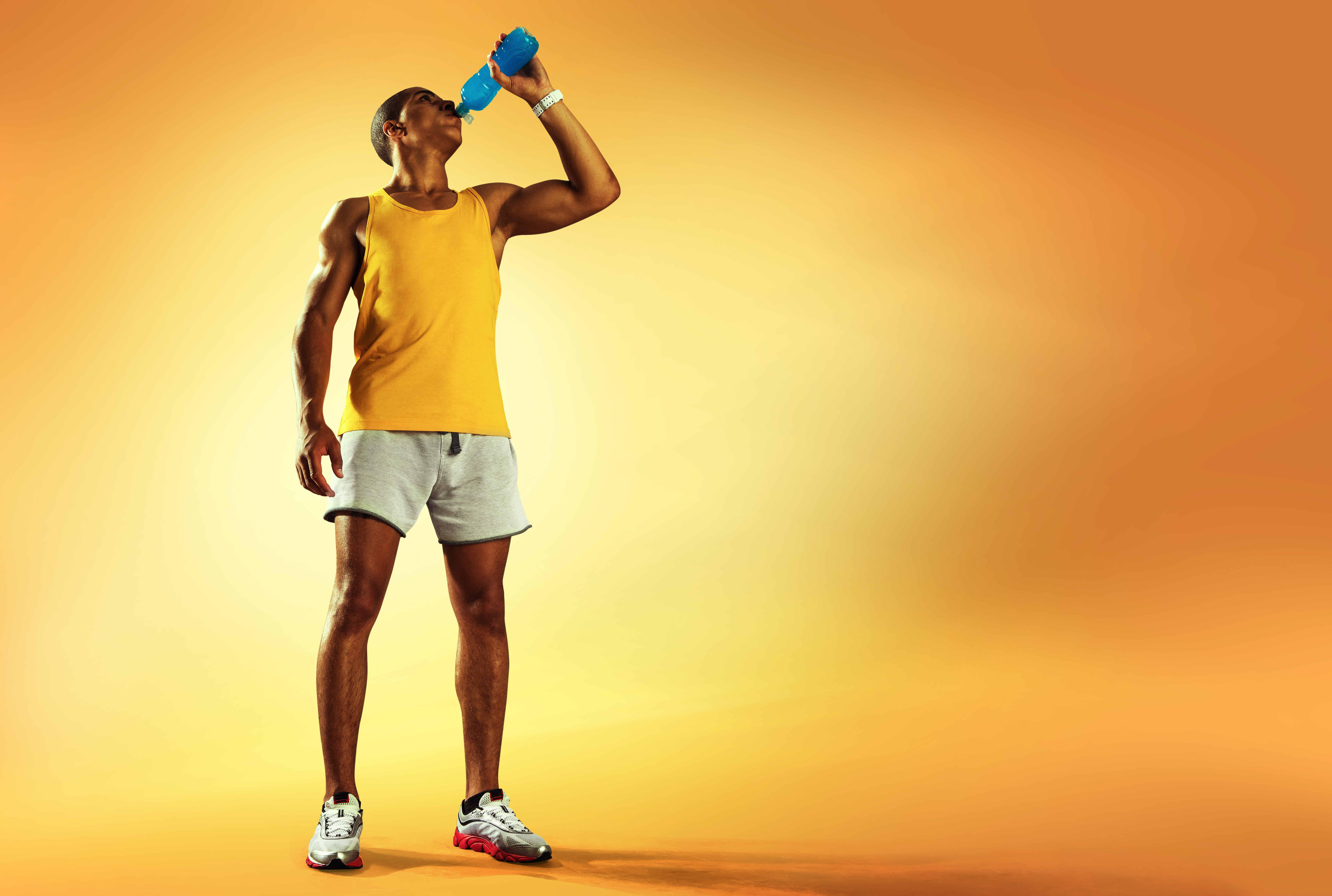 A man hydrating from a bottle on an orange background.