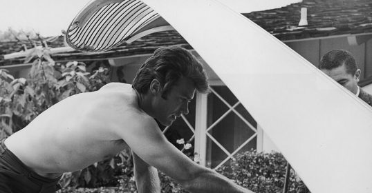 A man performing auto maintenance on a car engine with a shirt on.