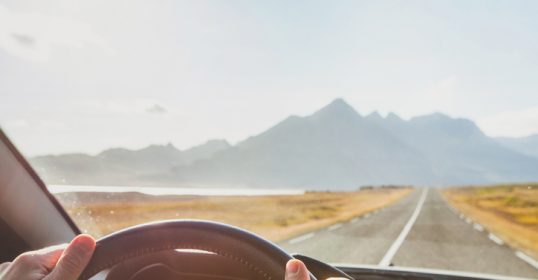 A person driving a car with mountains in the background.