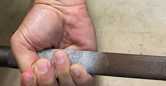 A person's hand holding a metal rod using the Hook grip technique.