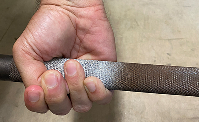 A person's hand holding a metal rod using the Hook grip technique.