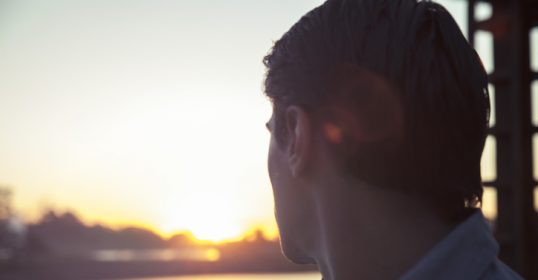 A man is looking out over a body of water, contemplating life's regrets.