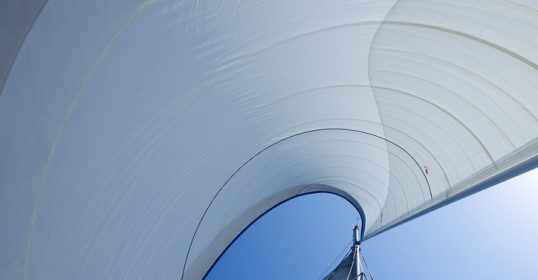 A view of a sailboat with a white sail, floating peacefully on the water.