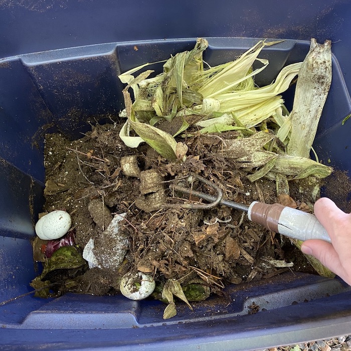 Forked garden tool is being used to stir the whole waste materials such as corn,eggs and nitrogen rich soil. 