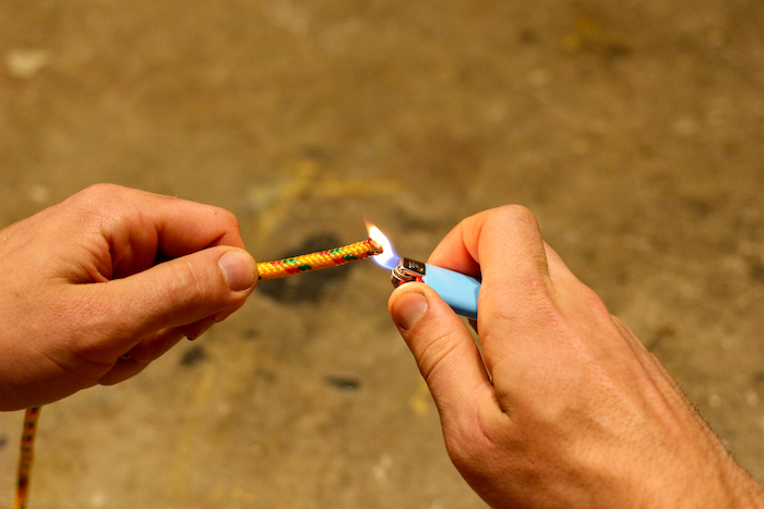 A man is burning a synthetic rope with lighter.