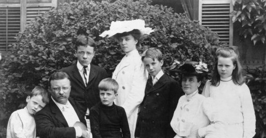A black and white photo of a family with children posing in front of a house.