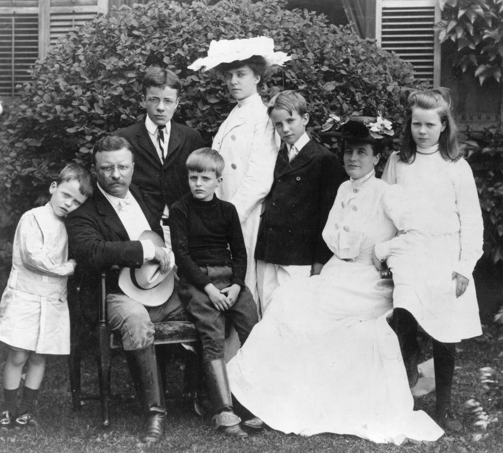 A black and white photo of a family with children posing in front of a house.