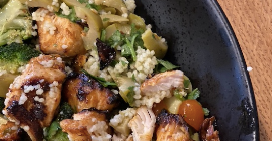 Quinoa salad with marinated chicken and vegetables in a black bowl.