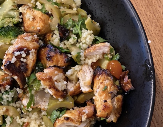Quinoa salad with marinated chicken and vegetables in a black bowl.