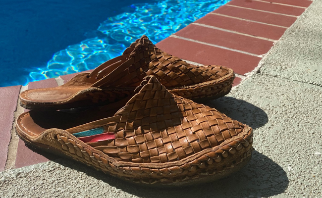 A pair of brown woven slippers by the pool during summertime.