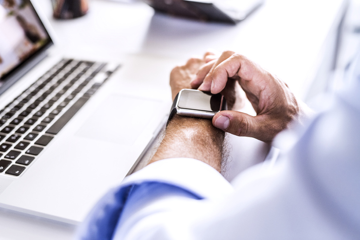 A man is using a smartwatch while working on a laptop.