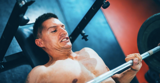 A man bench pressing a barbell with a spotter in the gym.