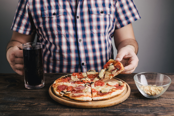 A man is holding a slice of pizza and a glass of beer, wondering what to do about overeating.