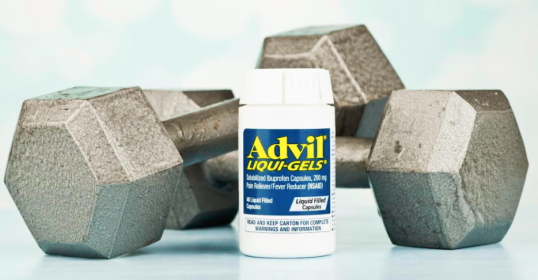 An ibuprofen bottle sits next to a set of dumbbells, ready to help with workouts.