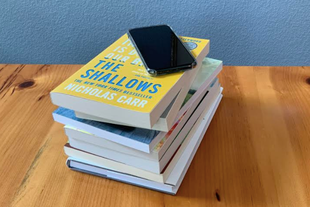 A stack of books with a cell phone on top, showcasing the intersection of traditional books and digital life.