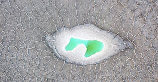 A shallow hole in the ground with green water.
