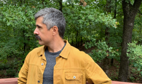 A man in a yellow fall jacket standing on a wooden deck.