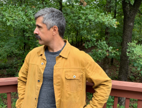A man in a yellow fall jacket standing on a wooden deck.
