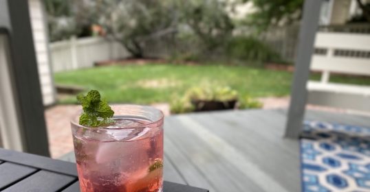 A pink drink on a table in front of a deck.