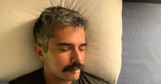 A man with a mustache sleeping in bed at night.