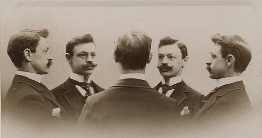 Four men in suits engaging in self-awareness exercises, observing each other closely.