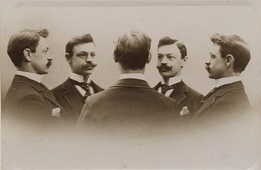 Four men in suits engaging in self-awareness exercises, observing each other closely.