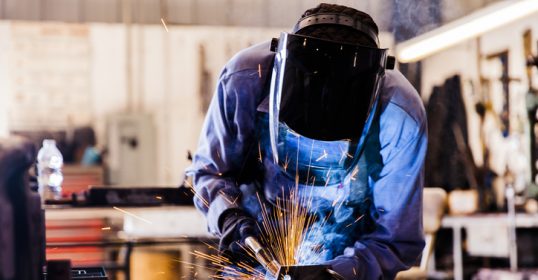 A senior man welds a metal part in his workshop.