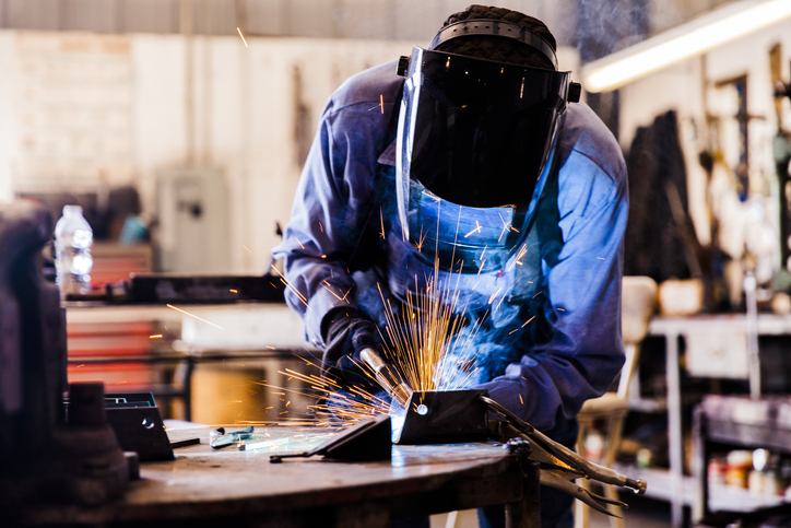 A senior man welds a metal part in his workshop.