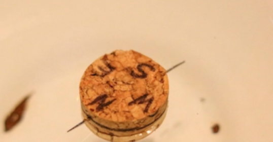 A wine cork in a white bowl with DIY writing on it.