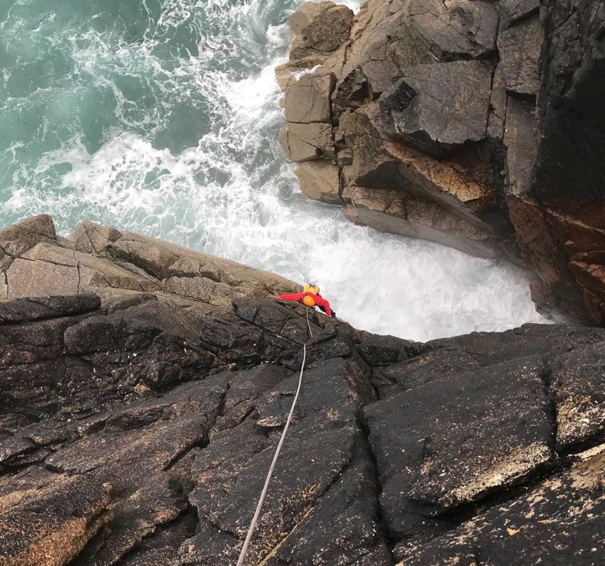 man climbing rock wall with water beneath. 