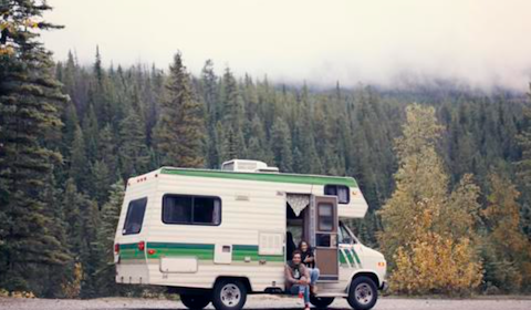 A white and green RV parked in a gravel lot, perfect for the dirtbag traveler.