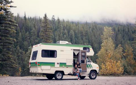 A white and green RV parked in a gravel lot, perfect for the dirtbag traveler.