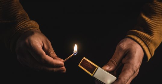 In front of a dark background, a pair of hands holds a lighter.