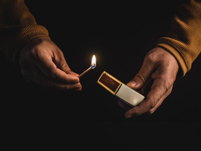 In front of a dark background, a pair of hands holds a lighter.