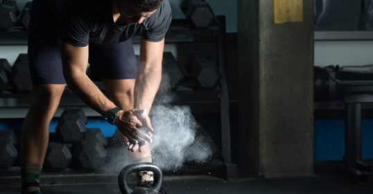 A man getting in shape at the gym by using powder on a kettlebell.