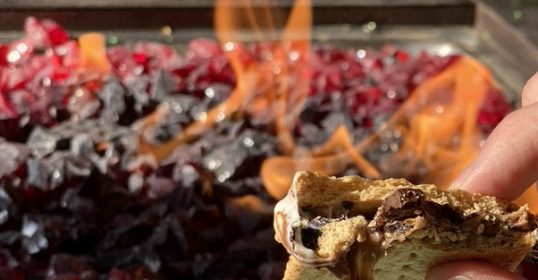 A person upgrading their s'more by the fire pit.