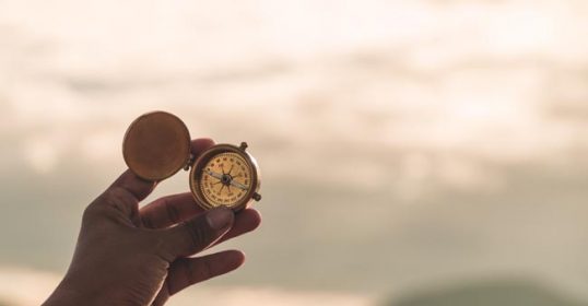 A person finding purpose as they hold a compass in front of a mountain.