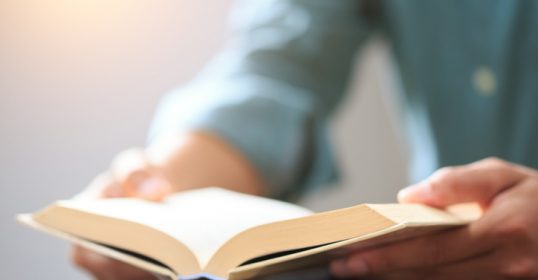 A person with a devotional reading habit is engrossed in a book at the table.