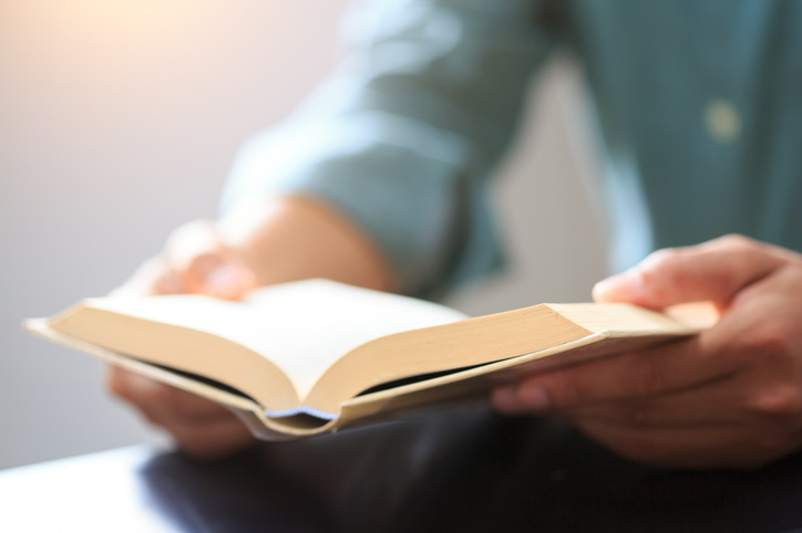 A person with a devotional reading habit is engrossed in a book at the table.