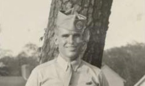 A man in uniform stands next to a tree, exuding steadiness and inspiration.