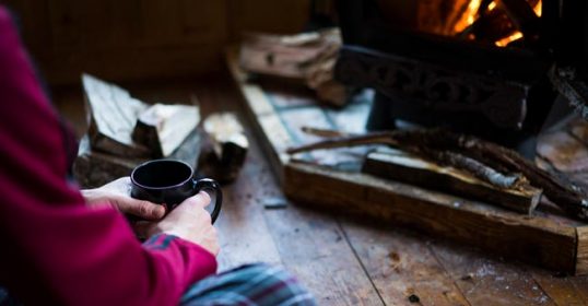 A person sitting in front of a fire with a cup of coffee, enjoying the hygge atmosphere.