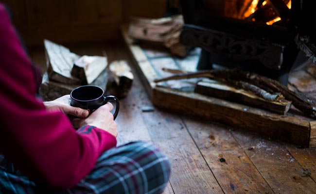 A person sitting in front of a fire with a cup of coffee, enjoying the hygge atmosphere.