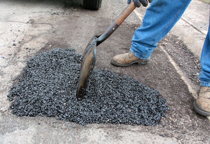 A man using a shovel to dig a hole in the road for maintenance.