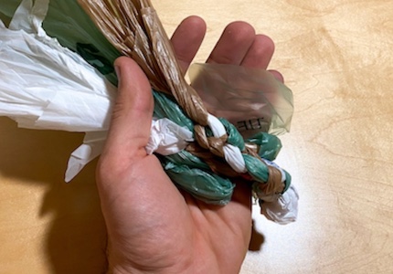 A hand holding a piece of plastic wrapped around a straw.
